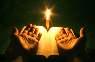 hands open before Bible and candle