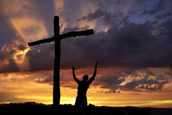 man kneeling with uplifted hands before cross